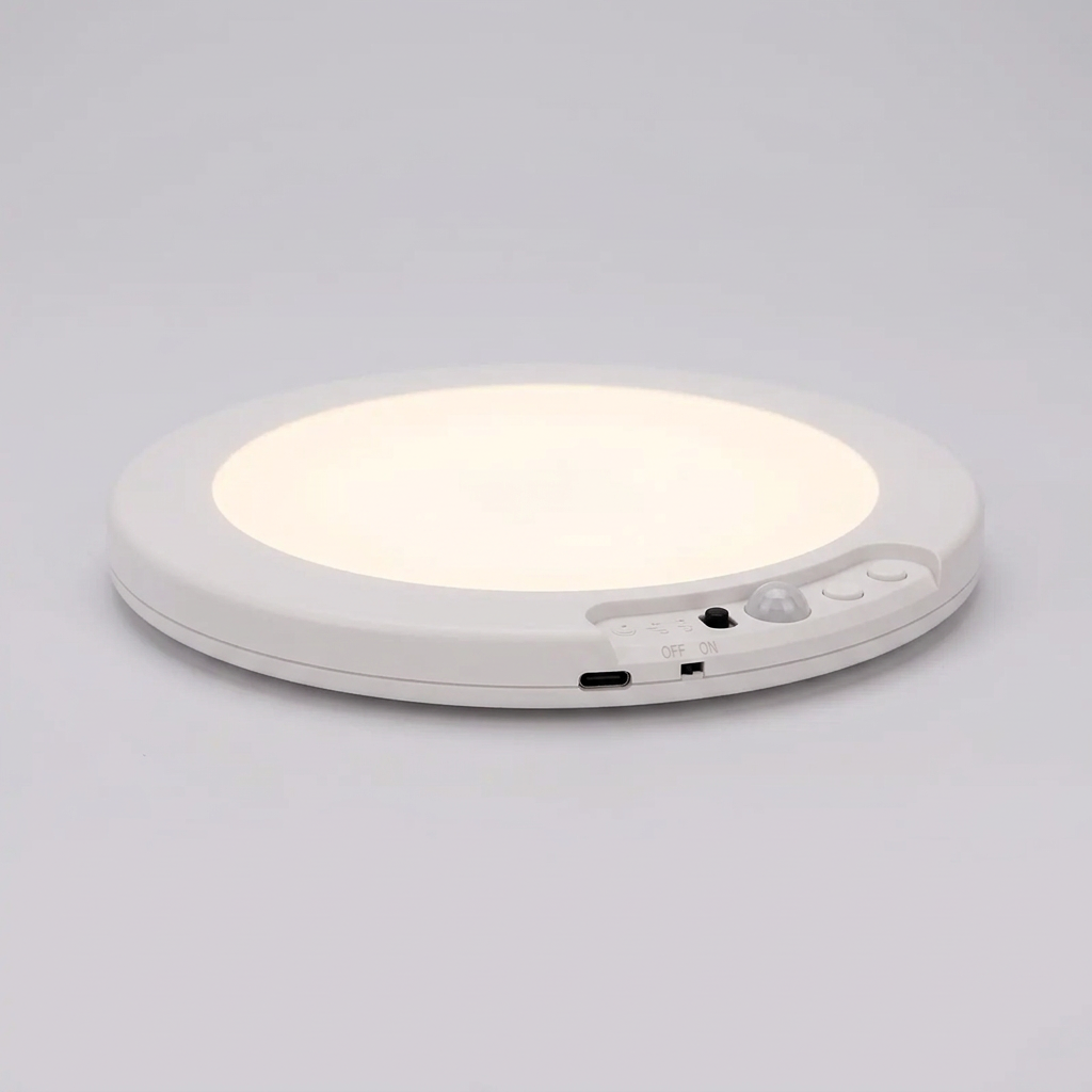 Rechargeable LED motion sensor ceiling light, slim white round design with sensor controls and USB-C port, glowing soft white against a grey background